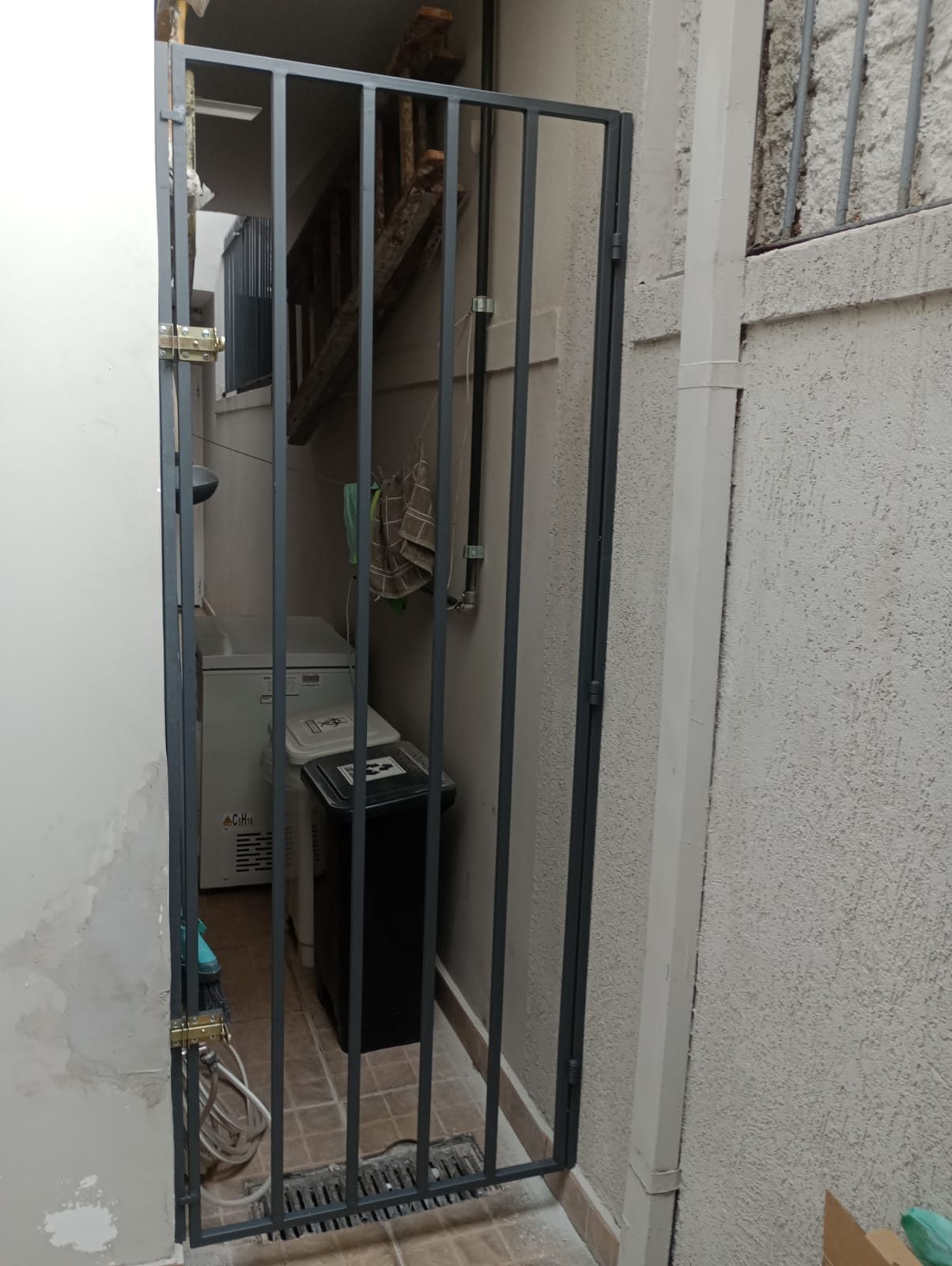 Portão social gradeado cinza instalado em corredor de residência em Moema, São Paulo